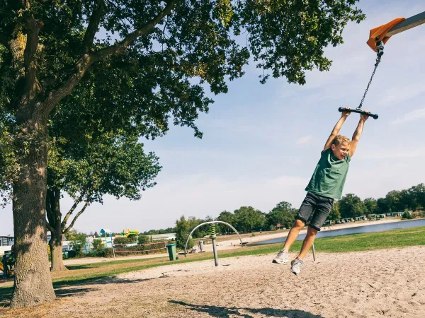 Kind slingert aan speeltouw in speeltuin bij Roan camping de Schatberg.