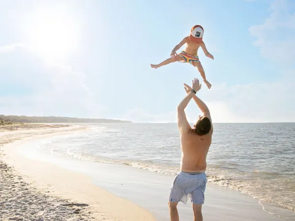 Vader gooit jongetje de lucht in op het strand bij Roan camping Sole Family Camping Village.