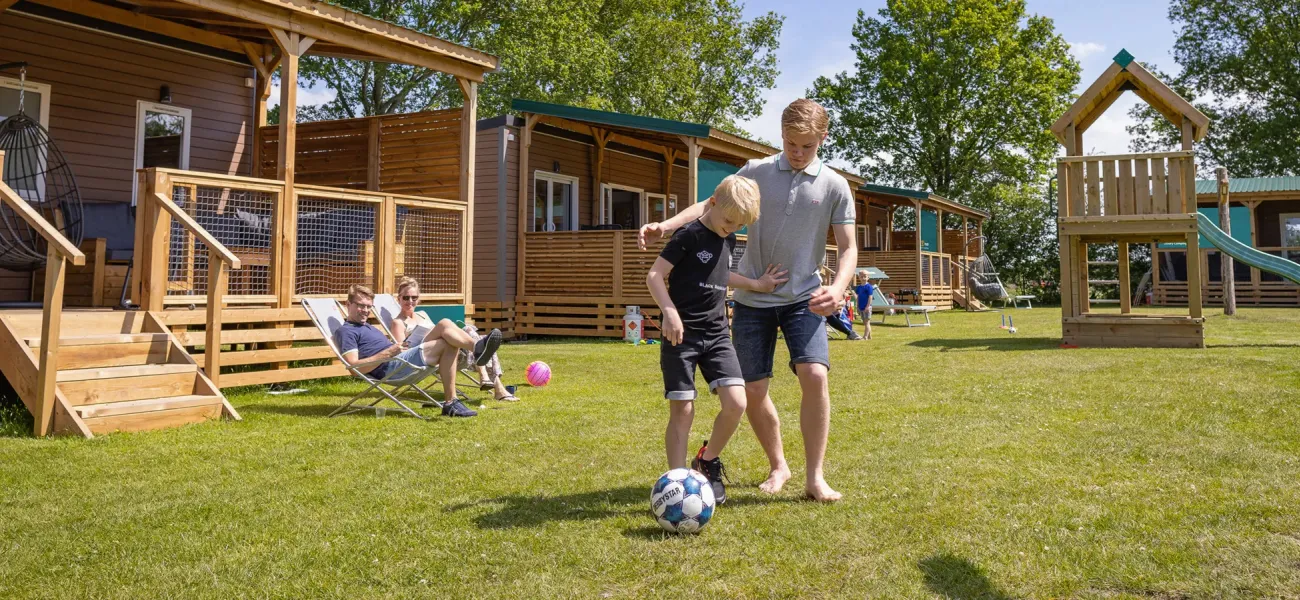 Kinderen die voetballen voor een stacaravan op een Roan camping.